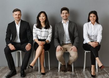 smiling interracial business people in formal wear looking at camera while waiting for job interview